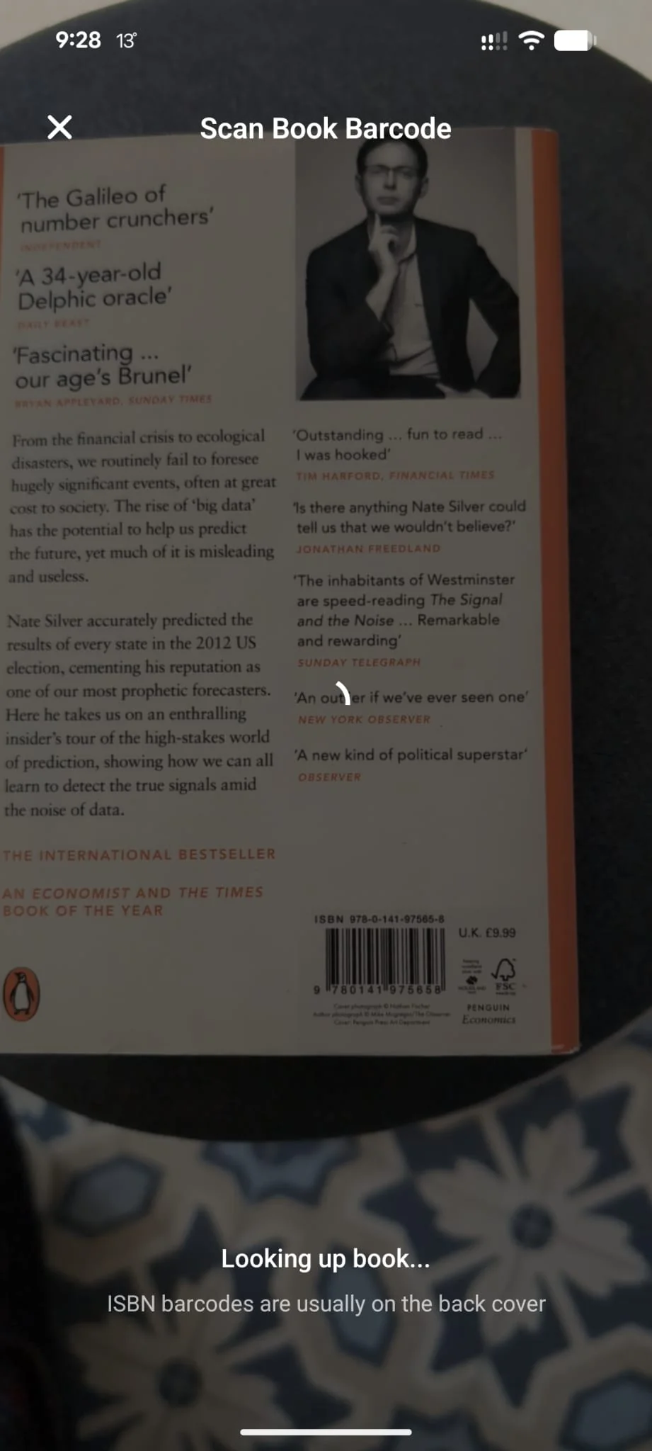 Shellf's Scan Book Barcode screen with the camera viewfinder pointed at the back cover of a Penguin paperback. The ISBN barcode is visible mid-frame, with a 'Looking up book...' status at the bottom and a hint reading 'ISBN barcodes are usually on the back cover'.
